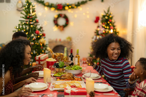 family moment during Christmas as they exchange gifts around festive dinner table. The table with Christmas-themed tableware, candles and delicious food. The room is adorned with holiday decorations.