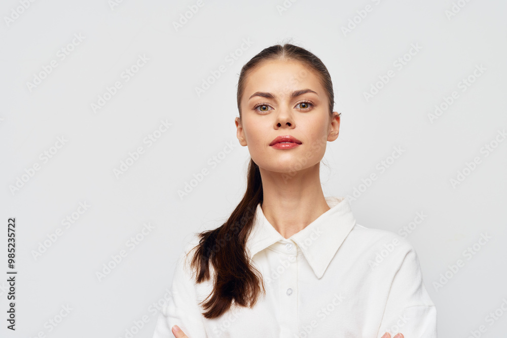Confident young woman with long brown hair, wearing a white shirt, standing against a neutral background, exuding self assurance and professionalism Confident young woman with long brown hair, wearing a white shirt, standing against a neutral background, exuding self assurance and professionalism