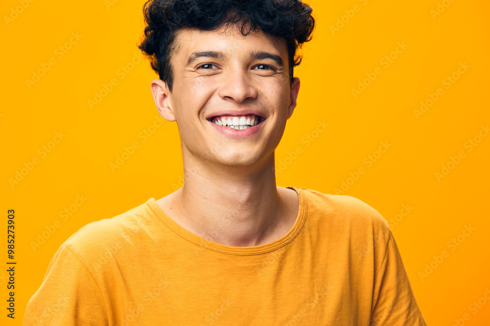 Smiling young man with curly hair on a bright yellow background, wearing a casual orange t shirt, radiating positivity and joy, perfect for lifestyle and happiness themes Smiling young man with curly hair on a bright yellow background, wearing a casual orange t shirt, radiating positivity and joy, perfect for lifestyle and happiness themes