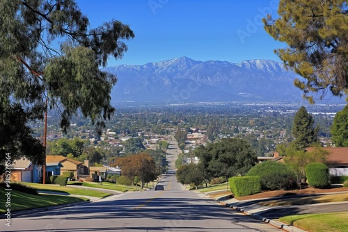 Serene suburban neighborhood with road, green trees, houses. Majestic San Gabriel Mountains rise in distance against clear blue sky, adding depth, scale. Vantage point, comprehensive view of photo