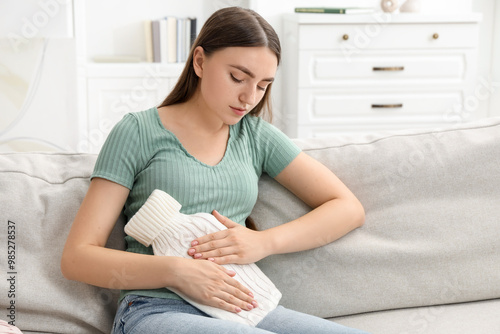 Woman using hot water bottle to relieve menstrual pain on sofa at home
