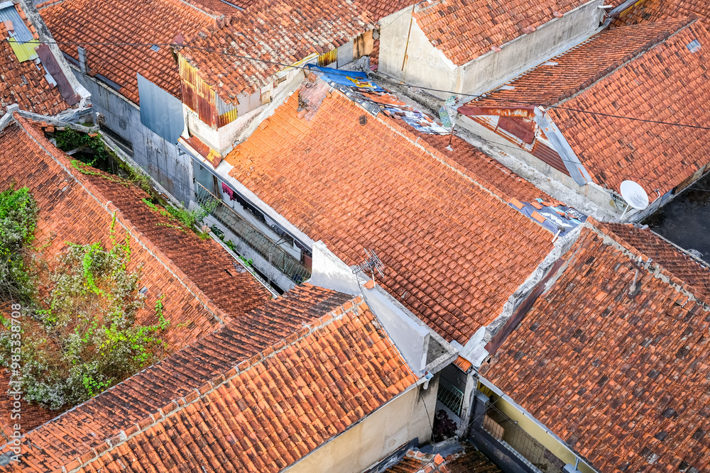 Residential houses in Java, Indonesia, with red-tiled roofs, lush greenery, and a cozy traditional atmosphere. Some roofs have overgrown plants, blending nature with urban living.