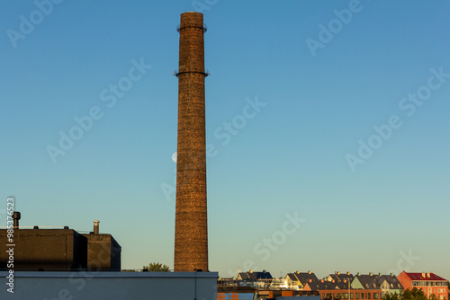 The moon hides behind a brick chimney above the roofs of Tallinn houses early in the morning