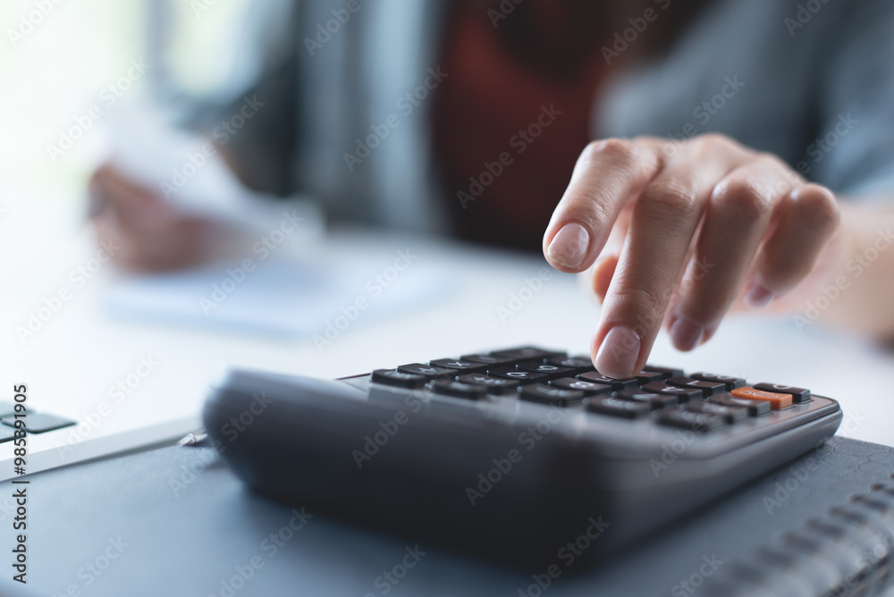 Doing finance, budgeting and tax calculation. Close up woman hand using calculator to calculate home finance, accounting with laptop computer on table, budget management, monthly expenses Doing finance, budgeting and tax calculation. Close up woman hand using calculator to calculate home finance, accounting with laptop computer on table, budget management, monthly expenses