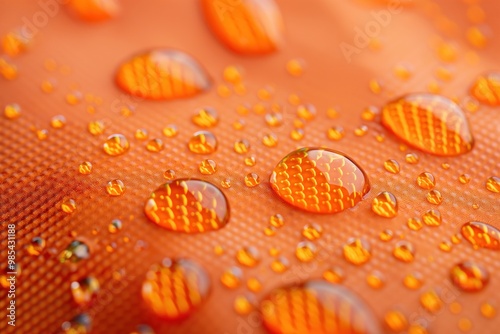 Vibrant orange fabric showcases water droplets beading up on its surface. Close-up view highlights texture and repelling properties of synthetic ripstop material. photo