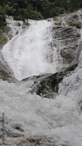 Waterfall in the rainforest of the Cameron Highlands, Malaysia. A rainforest river tumbles down the rocky abyss. Water splashes on the rocks. Masses of water poured over stones. Vertical real time