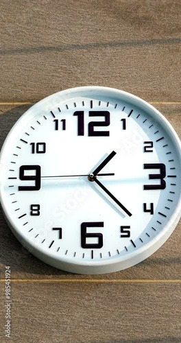 Close up to wall clock, with running time pointer. Sun and sky reflecting on clock face time passing by. Vertical time lapse on a modern white Clock on blur background. Wall clock show running time. 