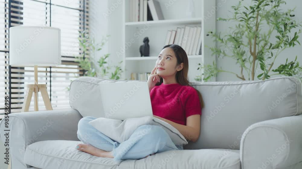 Happy young Asian woman using laptop while seated on couch at home Happy young Asian woman using laptop while seated on couch at home