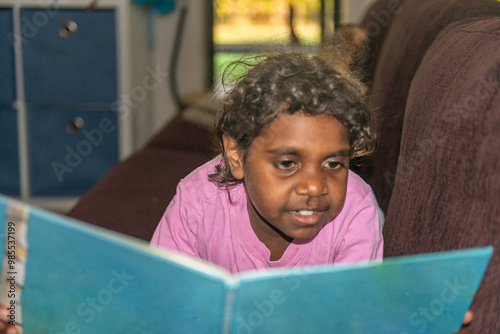 6 year old aboriginal girl reading a book focus behind subject photo