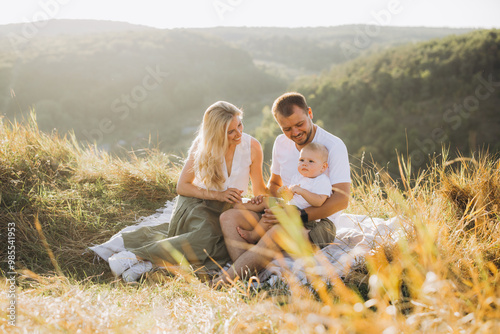 Foto Happy Family Having a Picnic in a Scenic Meadow with Sunlit Hills in the Backgro