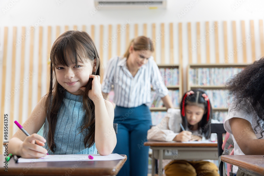 A girl is sitting at a desk with a teacher standing behind her A girl is sitting at a desk with a teacher standing behind her