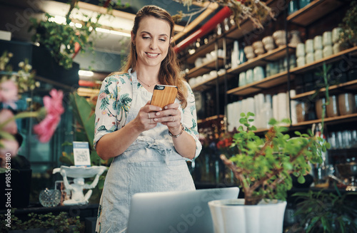 Laptop, phone and text message with florist woman at desk in small business for communication or ecommerce. Computer, sales and smile with happy employee in plant nursery for green retail startup