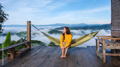 Portrait of a young woman sitting on hammock and looking at a mountain view and sea of fog