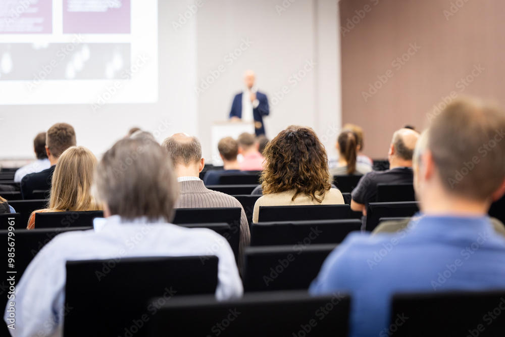 Rear view of the audience at a business conference meeting event listening to the speakers speech Rear view of the audience at a business conference meeting event listening to the speakers speech