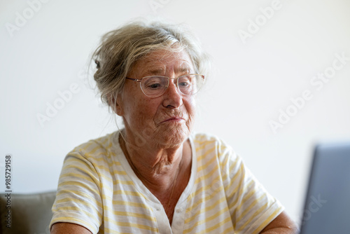 Senior woman works on the laptop and looks at it very skeptically photo