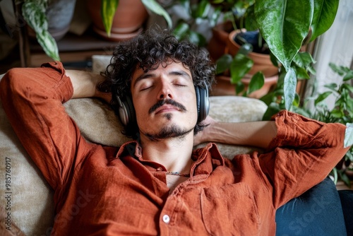 Urban Jungle Serenity: Young man finds peace amidst houseplants, eyes closed, lost in the rhythm of music playing through headphones photo