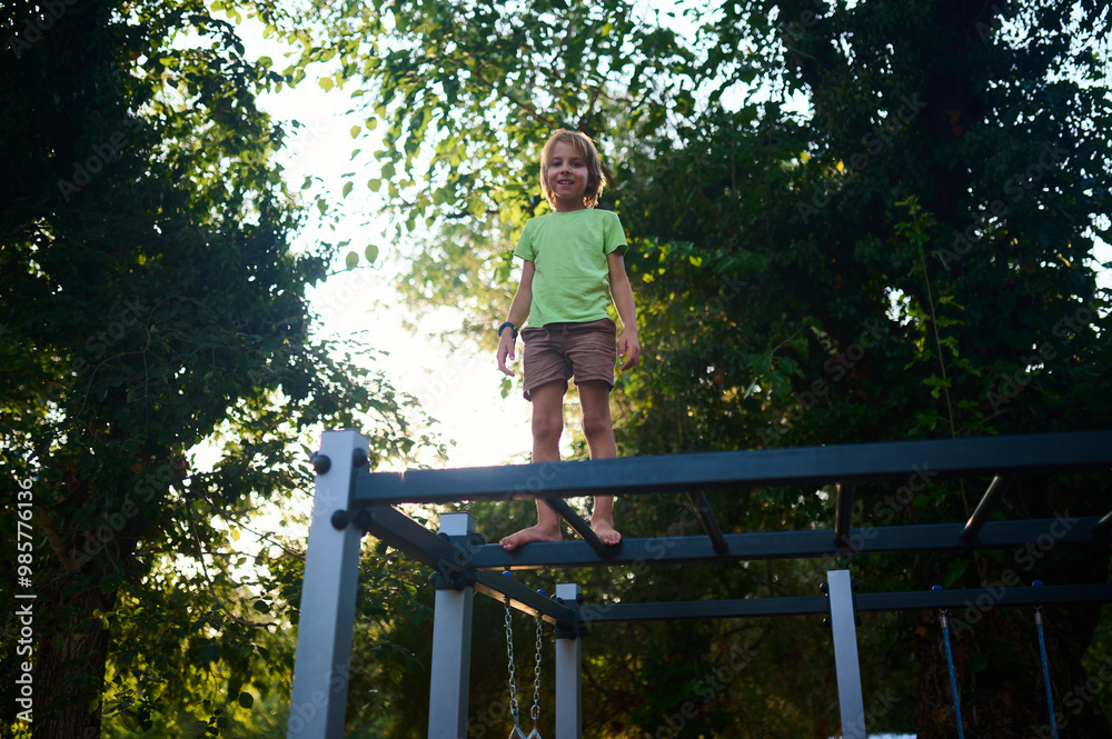 A child joyfully stands on a playground structure surrounded by lush greenery in the late afternoon sunlight A child joyfully stands on a playground structure surrounded by lush greenery in the late afternoon sunlight