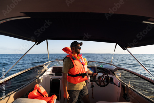 Bild auf Leinwand A young man of European appearance in a life jacket relaxes on a boat in the Baltic Sea on a summer day