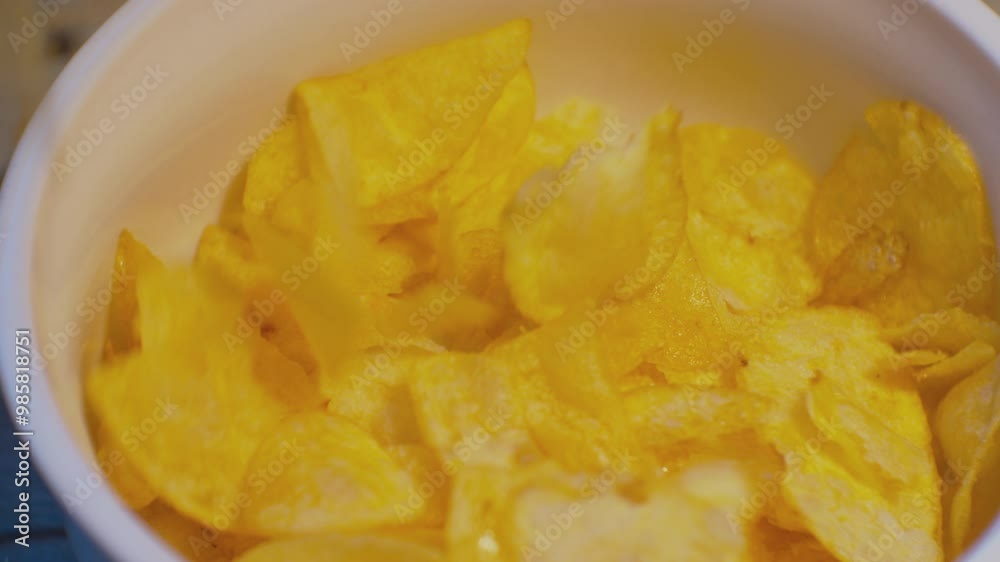 Appetizing yellow potato chips pour out of a pack into a cup. Close-up. Appetizing yellow potato chips pour out of a pack into a cup. Close-up.