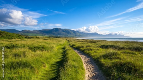 A scenic hiking trail winds through rolling green dunes and leads to breathtaking views of the Irish coastline with majestic mountains in the background.