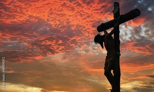 Silhouette of a man crucified on a cross against a fiery sunset sky