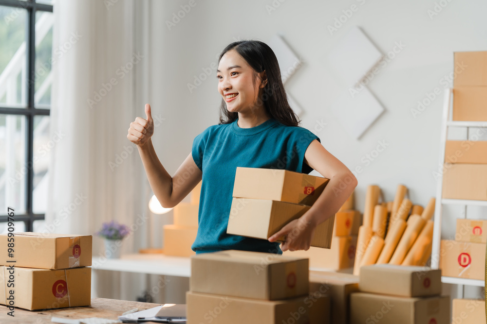 E-commerce Success: A young Asian entrepreneur celebrates a successful shipment, giving a thumbs-up amidst a flurry of packages in her bustling home office. E-commerce Success: A young Asian entrepreneur celebrates a successful shipment, giving a thumbs-up amidst a flurry of packages in her bustling home office.