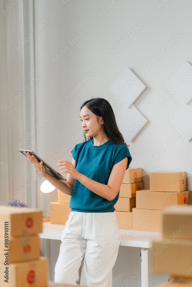 Young Entrepreneur Managing Orders: A young woman in a teal t-shirt and white pants stands in her home office, using a tablet to manage orders for her online business. The image captures the hustle an Young Entrepreneur Managing Orders: A young woman in a teal t-shirt and white pants stands in her home office, using a tablet to manage orders for her online business. The image captures the hustle an