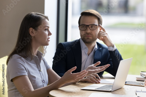 Serious business colleagues negotiating on deal, project, startup, discussing cooperation. Businesswoman speaking at corporate meeting, looking away, sitting at table with laptop