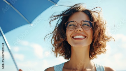 A cheerful young woman with curly hair holds a blue umbrella, smiling brightly on a clear sunny day, embodying joy, optimism, and freedom.