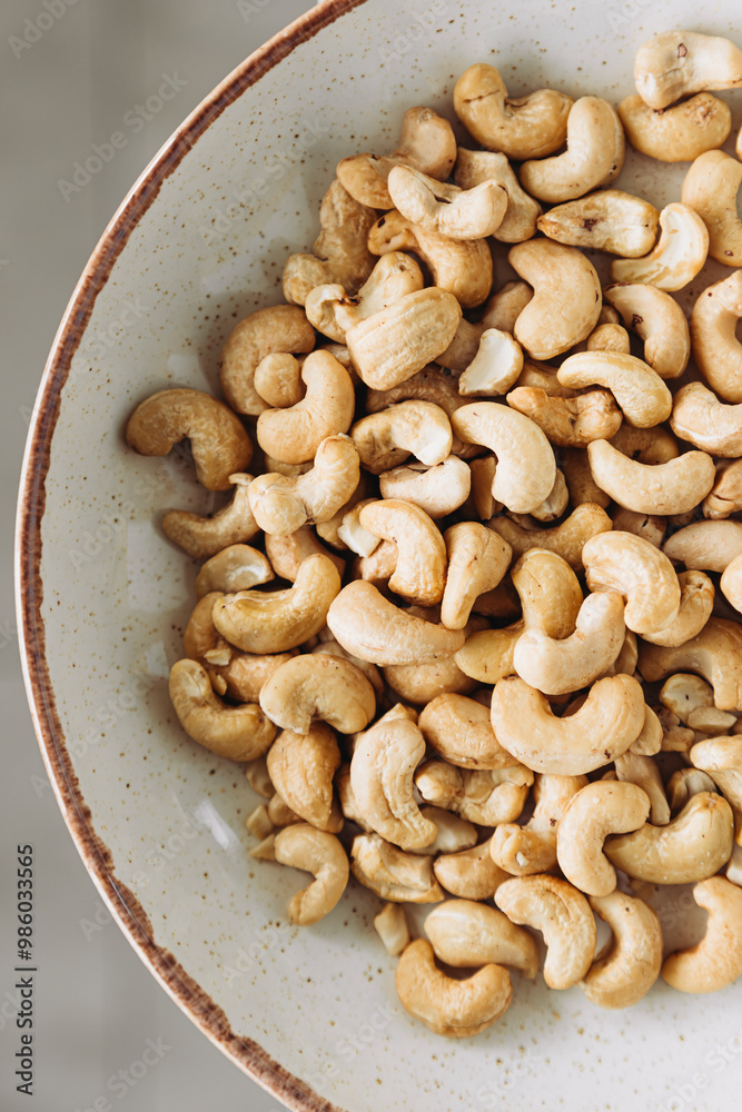 Cashew nuts are poured into white plate on table, close up still life. Cashew nuts are poured into white plate on table, close up still life.