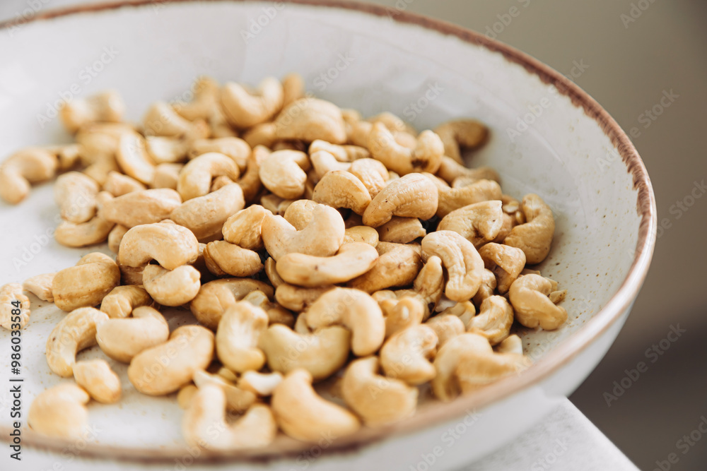 Cashew nuts are poured into white plate on table, close up still life. Cashew nuts are poured into white plate on table, close up still life.