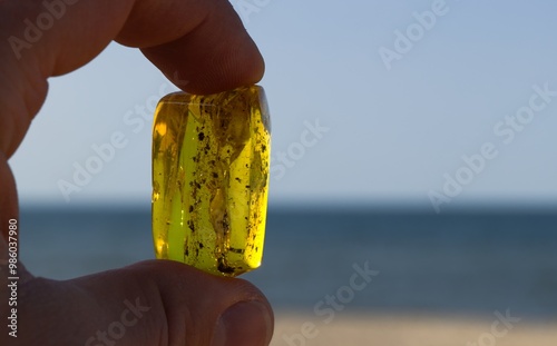 Fototapeta Naklejka Na Ścianę i Meble -  Close-up of a man’s hand gripping a smooth, transparent Baltic amber between two fingers, glowing softly in the light.