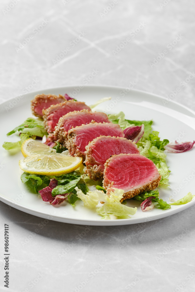 Freshly prepared seared tuna slices on a bed of greens with lemon wedges ready to eat Freshly prepared seared tuna slices on a bed of greens with lemon wedges ready to eat