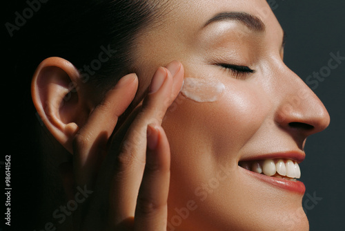 Enjoying young woman applying moisturizer on her face