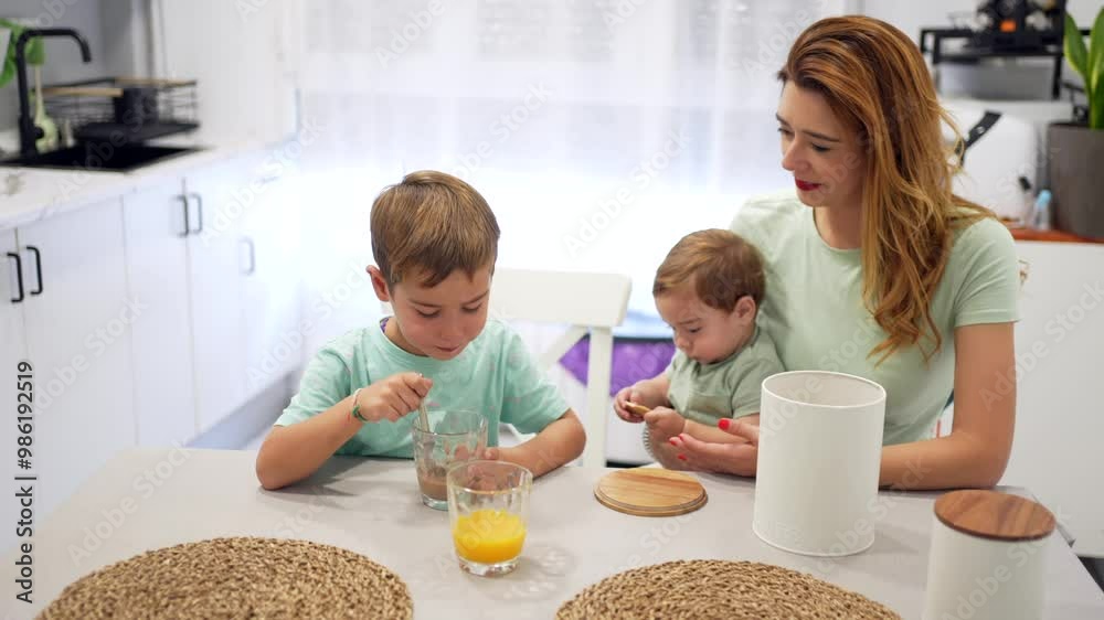 Happy woman feeding her son while holding a baby during breakfast at home