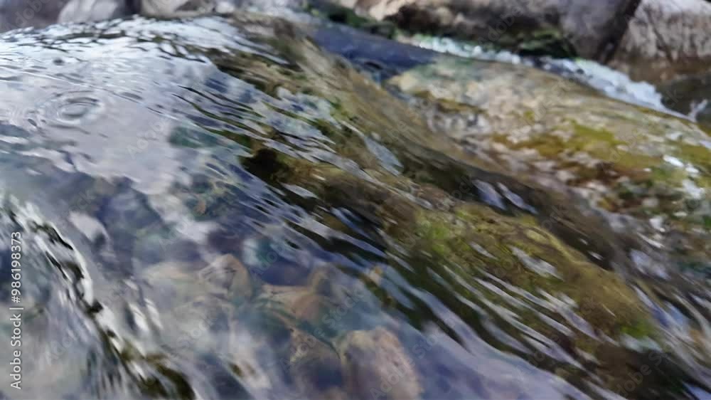 A slow-motion video capturing a small waterfall in a mountain stream. The water cascades gently over rocks, with each droplet and ripple accentuated, creating a tranquil and calming scene in nature. A slow-motion video capturing a small waterfall in a mountain stream. The water cascades gently over rocks, with each droplet and ripple accentuated, creating a tranquil and calming scene in nature.
