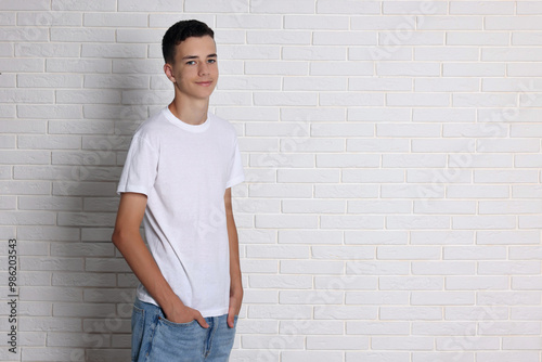 Teenage boy wearing t-shirt near white brick wall, space for text