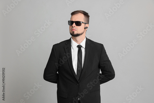 Young bodyguard in suit and sunglasses on grey background