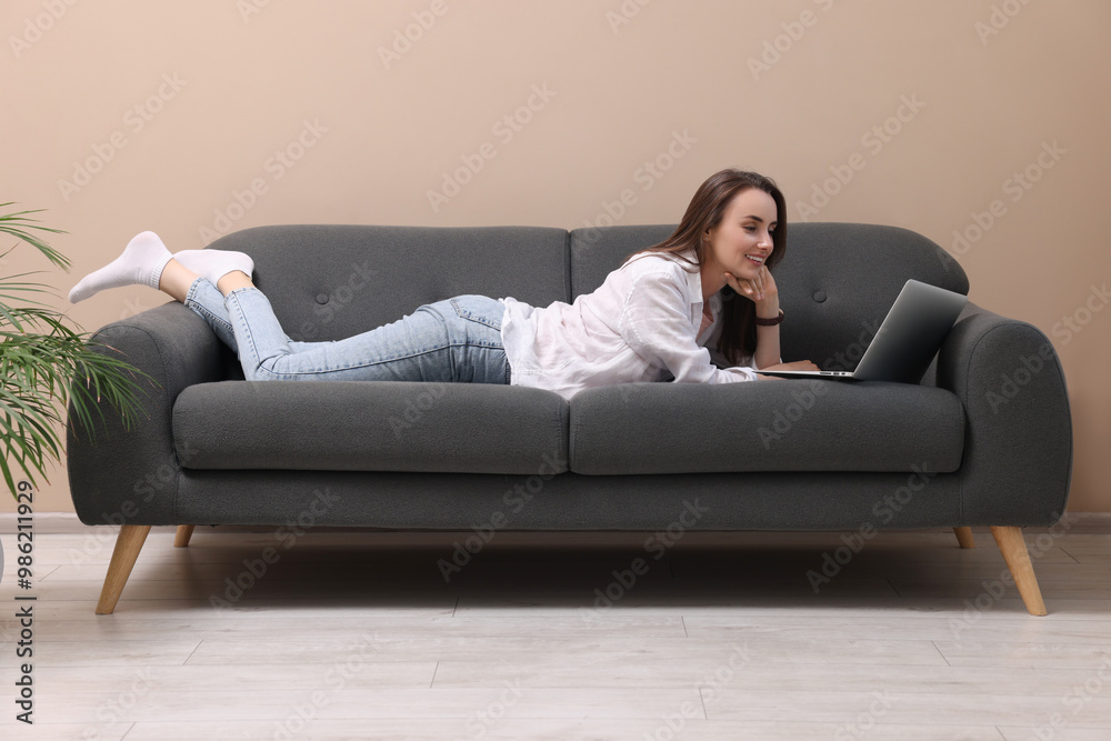 Smiling woman with laptop lying on sofa at home Smiling woman with laptop lying on sofa at home