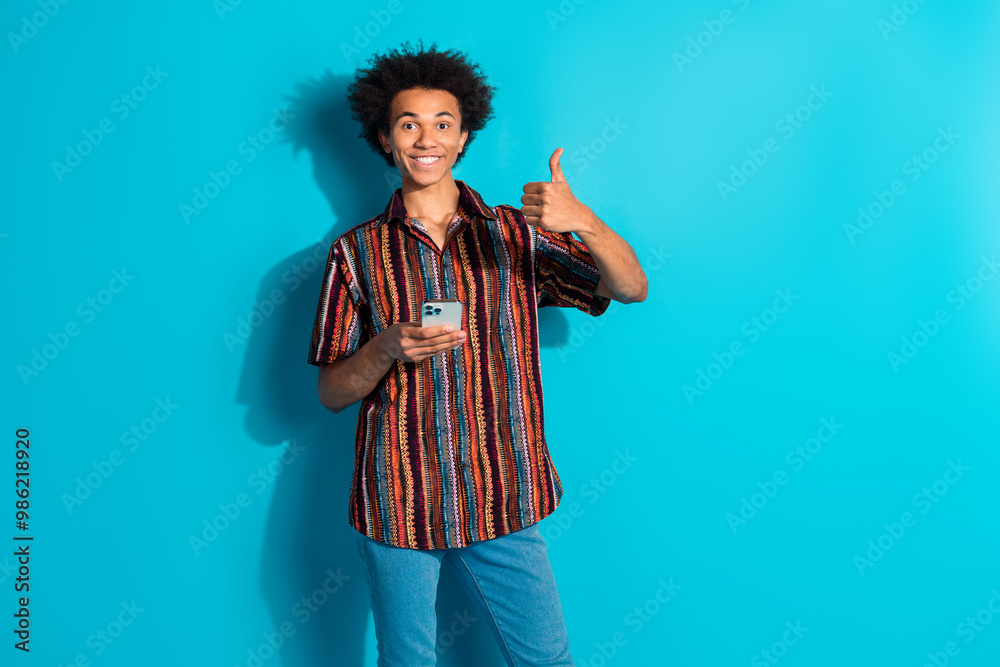 Portrait of nice young man thumb up phone wear shirt isolated on turquoise color background Portrait of nice young man thumb up phone wear shirt isolated on turquoise color background
