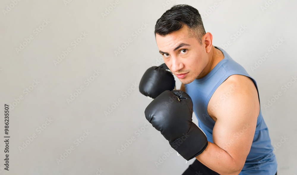 Hispanic male athlete with strong muscles wearing boxing gloves while training in a boxing studio Hispanic male athlete with strong muscles wearing boxing gloves while training in a boxing studio