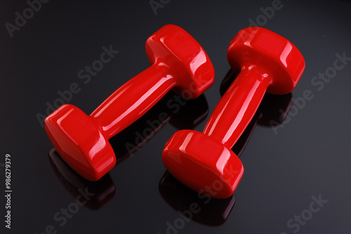 A pair of shiny dumbbells with bright highlights on a black mirror background. Close-up. View from above.