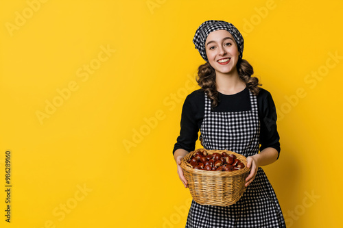 Smiling young chestnuts seller in checkered apron holding a basket of chestnuts on a yellow background photo