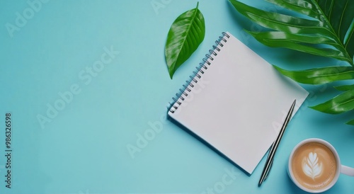 A cozy workspace featuring a coffee cup, a notepad, and a green leaf on a lig...