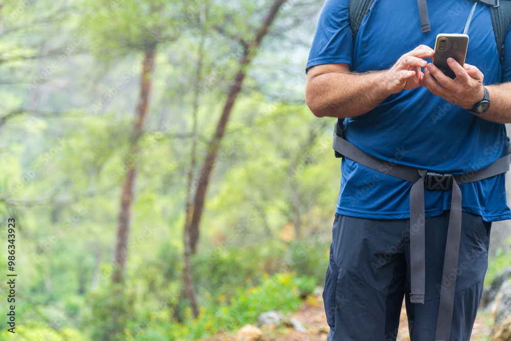 Unrecognizable hiker using the smarphone in the forest, touching the screen.