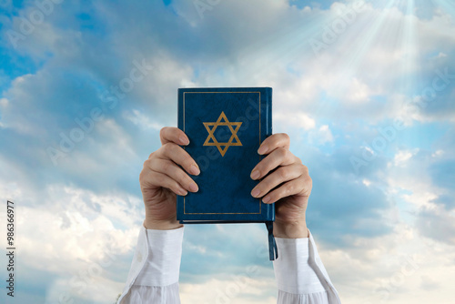 Hands and Hebrew Book Talmud with Star of David on a dark cover against the sky. Rabbinic Judaism, Studying Jewish religious law. Torah, Hebrew Bible. Holy Scripture containing the word of God photo