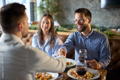 Happy businessmen shaking hands on a casual meeting at a restaurant while their female colleague is next to them. photo