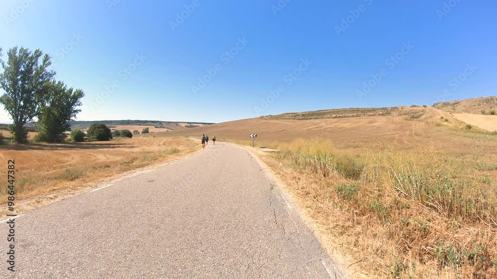 French Way of Saint James - pilgrims walking a paved road near Cardenuela Riopico, comarca of Alfoz de Burgos, province of Burgos, Castile and Leon, Spain French Way of Saint James - pilgrims walking a paved road near Cardenuela Riopico, comarca of Alfoz de Burgos, province of Burgos, Castile and Leon, Spain