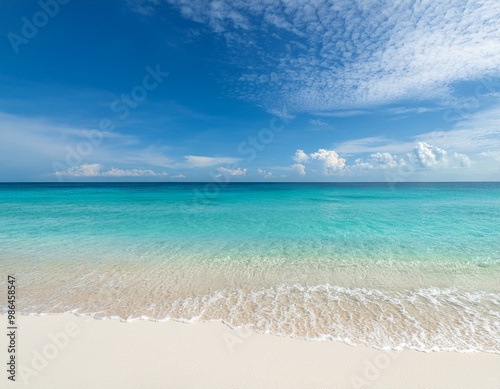 A serene beach scene with clear blue water lapping at a white sandy shore under a bright blue sky with fluffy clouds.