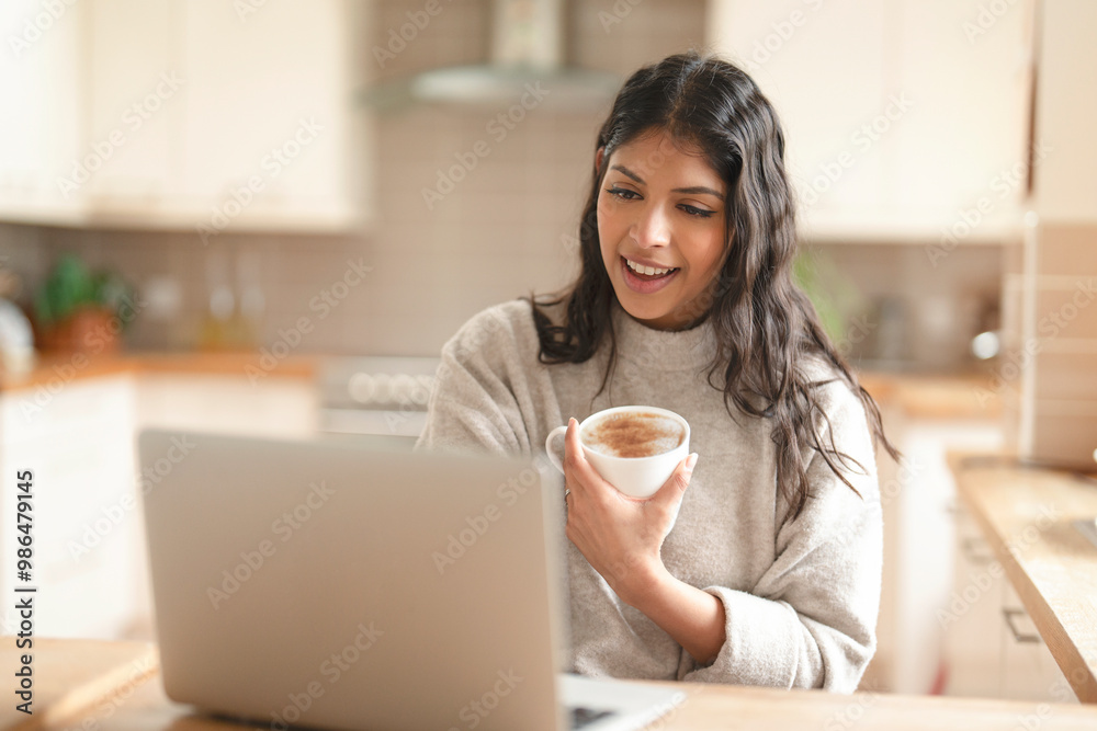 Young Woman Enjoying Warm Drink While Video Chatting in Cozy Kitchen Setting Young Woman Enjoying Warm Drink While Video Chatting in Cozy Kitchen Setting